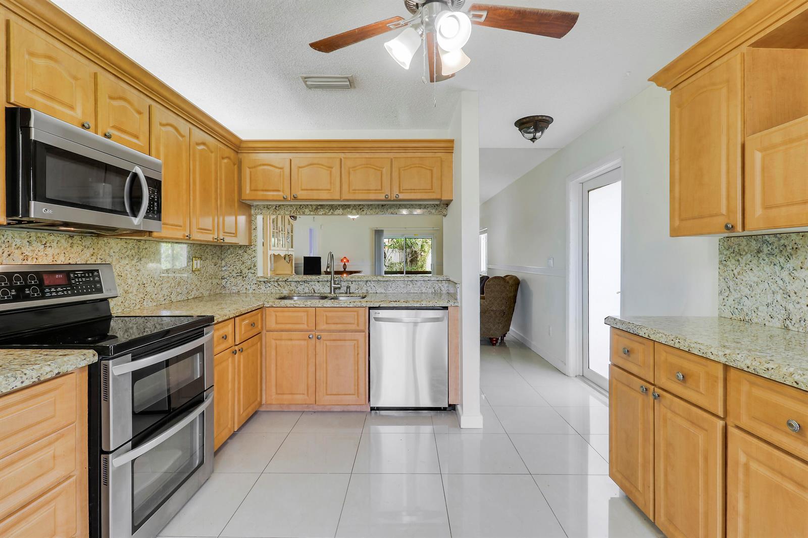 A kitchen with light wood cabinets, granite countertops, stainless steel appliances, and white tile flooring — 5373 Gene Circle, West Palm Beach FL 33415, WEST PALM BEACH, FL