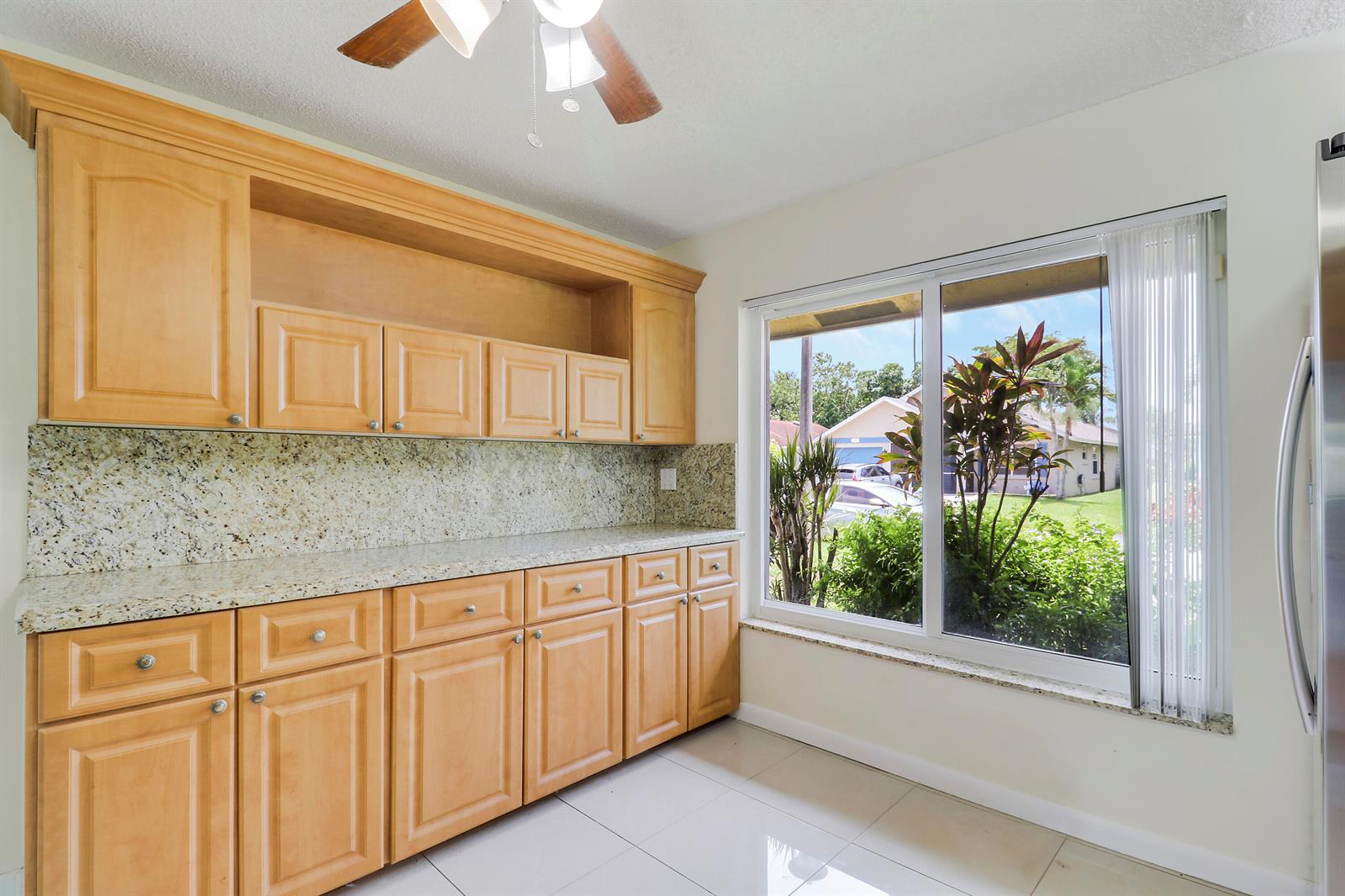 A kitchen features light wood cabinets, granite countertops, and a large window overlooking a yard — 5373 Gene Circle, West Palm Beach FL 33415, WEST PALM BEACH, FL