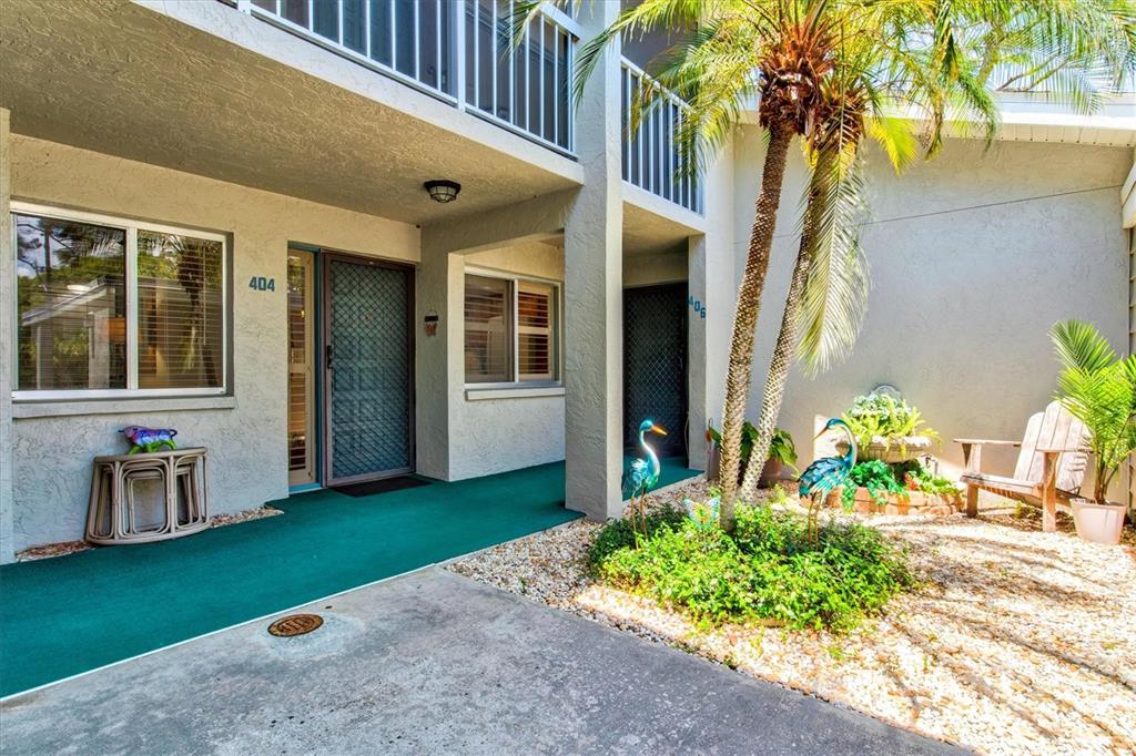 The exterior of a two-story apartment building features a green walkway and a small garden — 404 PINEBROOK CRESCENT UNIT 4, VENICE, FL