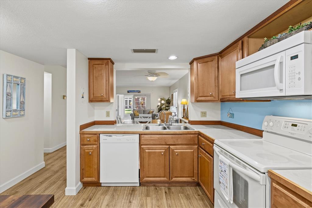 A kitchen with wood cabinets, white appliances, and a view into the living area — 404 PINEBROOK CRESCENT UNIT 4, VENICE, FL