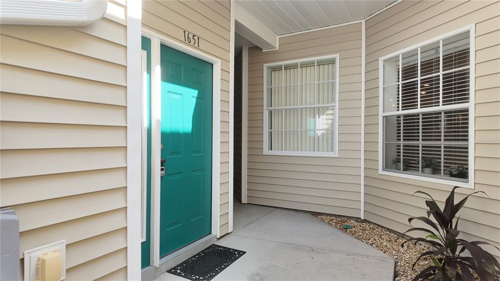 A teal front door with the number 1651 above it sits on a beige-sided porch — 1651 HAMMOCKS AVENUE, LUTZ, FL