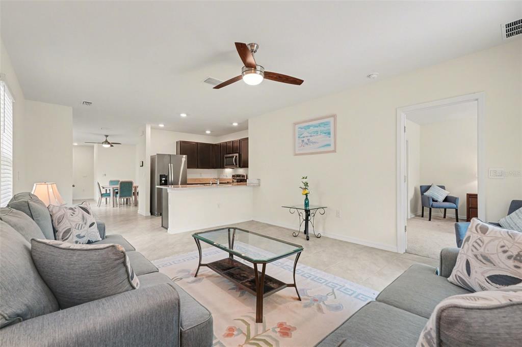 A living room with gray sofas and a glass coffee table opens to a kitchen — 3296 SUNCOAST PLAINS DRIVE, ODESSA, FL