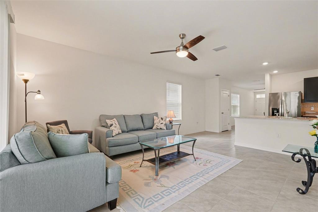 A living room with light tile floors, a blue sofa, and an open kitchen area — 3296 SUNCOAST PLAINS DRIVE, ODESSA, FL