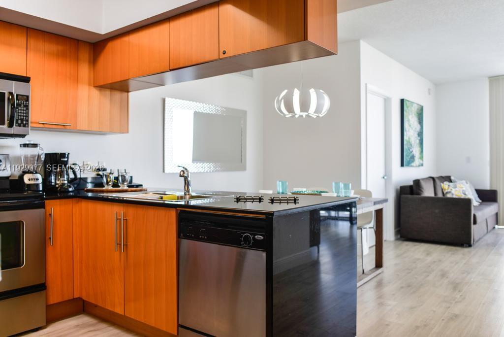 A kitchen with wood cabinets and black countertops opens into a living area with flooring — 1750 N Bayshore Dr # 4814, Miami FL 33132, MIAMI, FL