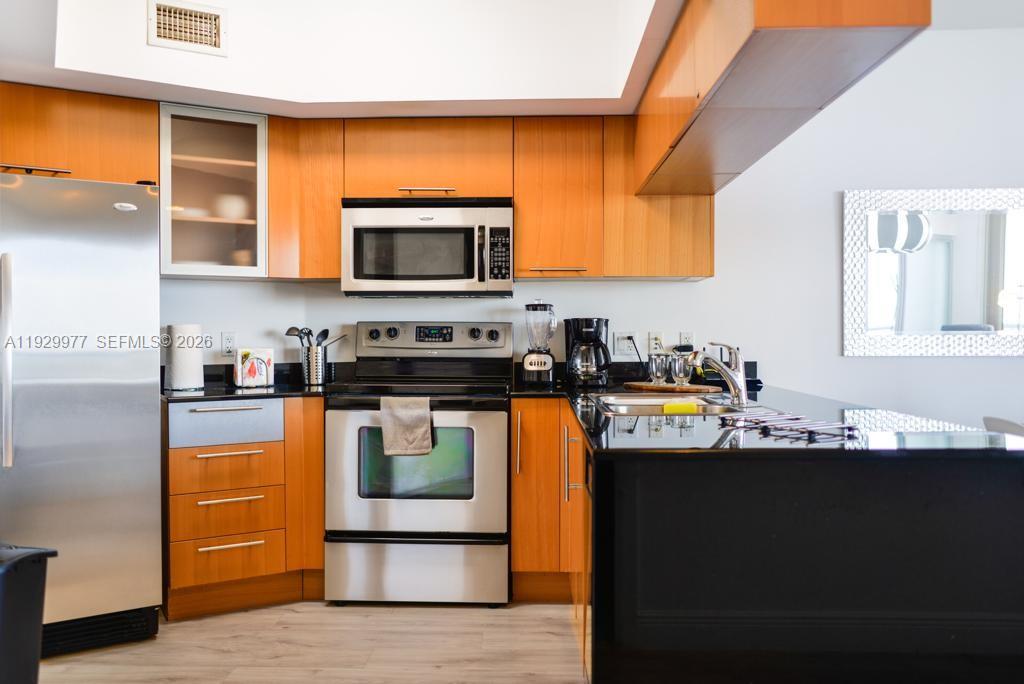 A kitchen features wood cabinets, stainless steel appliances, and black countertops — 1750 N Bayshore Dr # 4814, Miami FL 33132, MIAMI, FL
