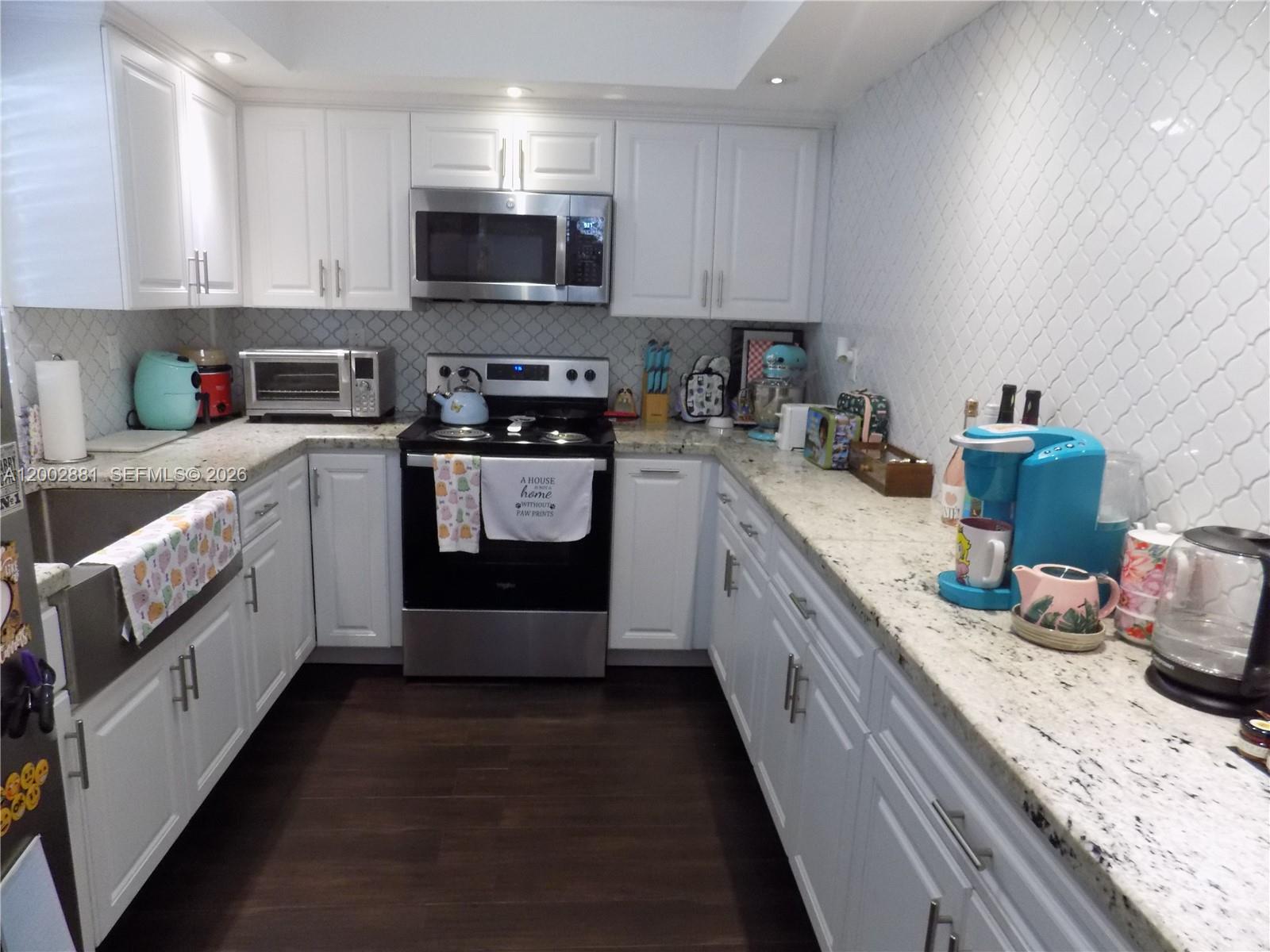 A galley kitchen features white cabinets, granite countertops, stainless steel appliances, and dark wood flooring — 20831 San Simeon Way # 103, Miami FL 33179, MIAMI, FL