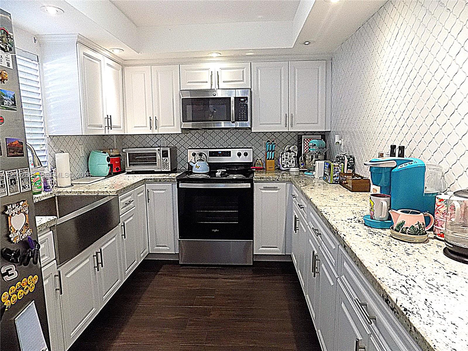A kitchen features white cabinets, granite countertops, stainless steel appliances, and a farmhouse sink — 20831 San Simeon Way # 103, Miami FL 33179, MIAMI, FL