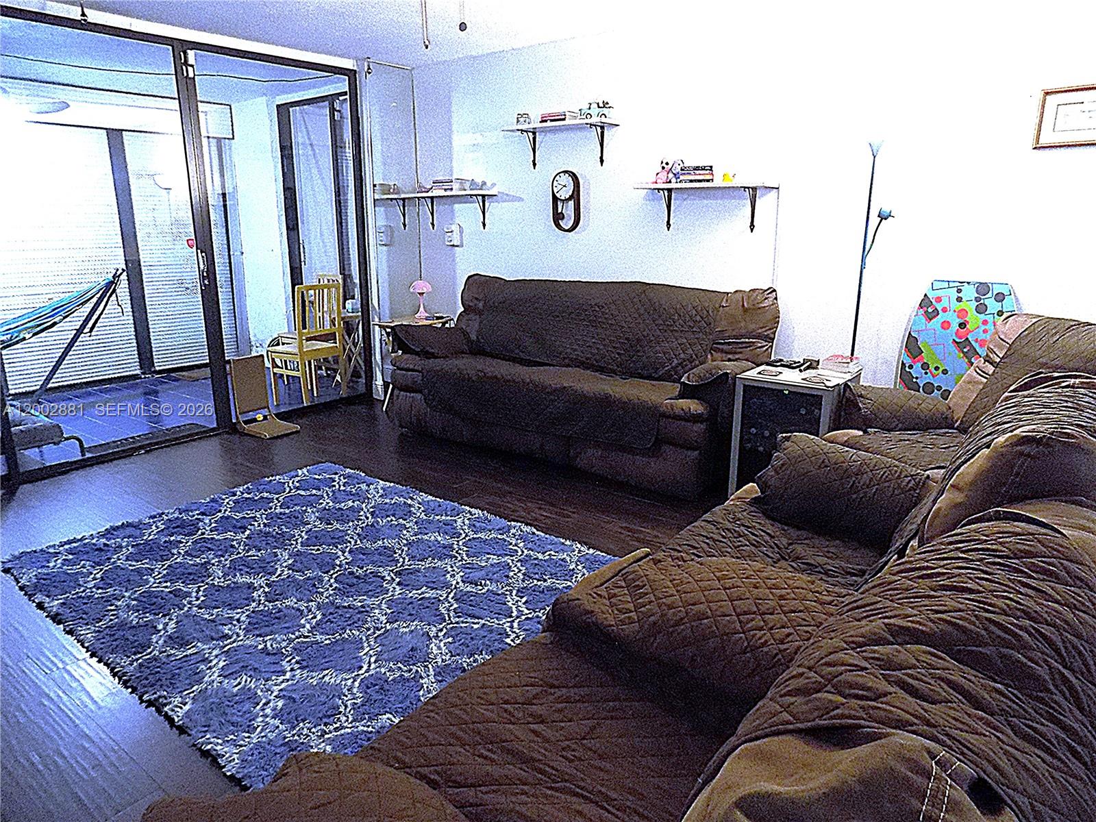 A living room features a blue patterned rug, brown sofas, and a sliding glass door — 20831 San Simeon Way # 103, Miami FL 33179, MIAMI, FL