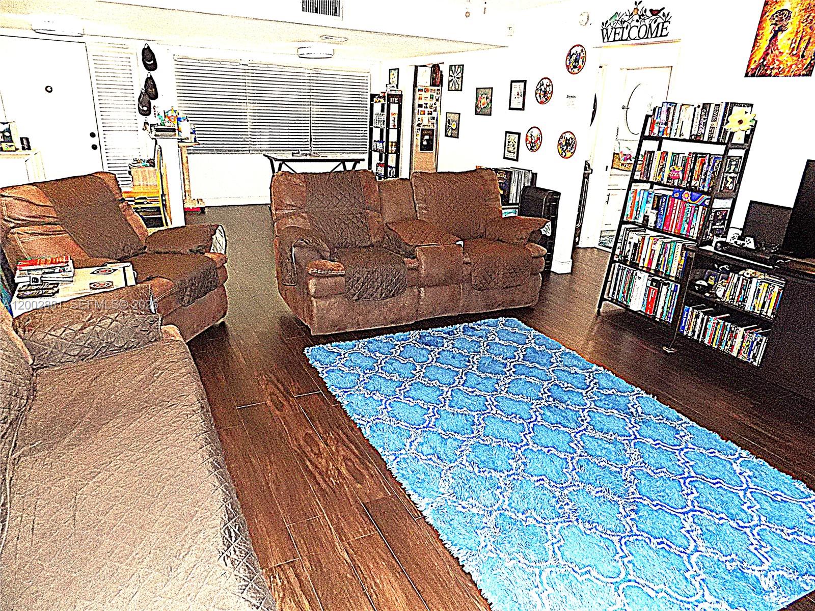 A living room features brown furniture, a bright blue patterned rug, and a tall bookshelf — 20831 San Simeon Way # 103, Miami FL 33179, MIAMI, FL