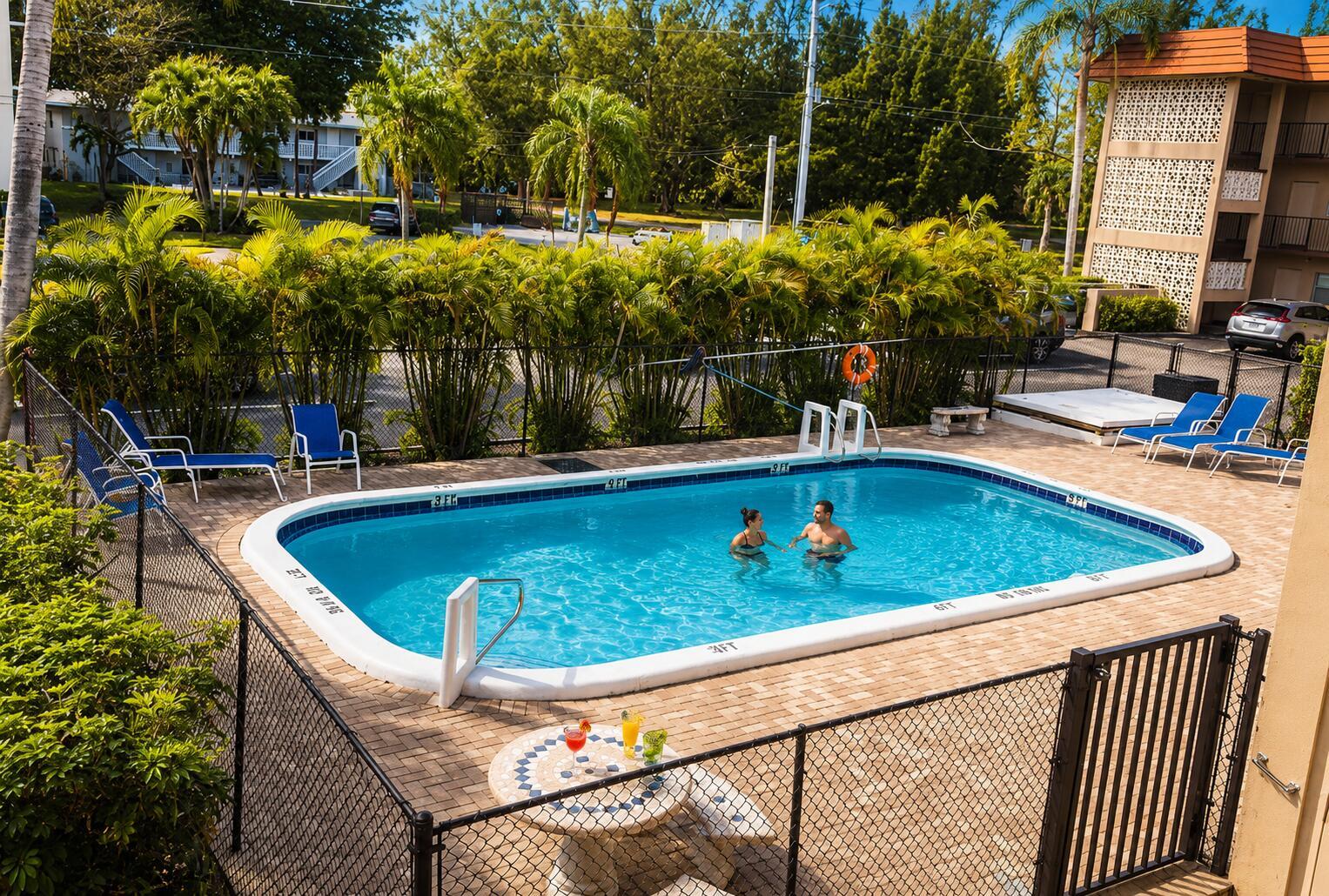 An outdoor swimming pool with a patio, lounge chairs, and a small table with drinks — 3930 Crystal Lake Drive # 206, Deerfield Beach FL 33064, DEERFIELD BEACH, FL