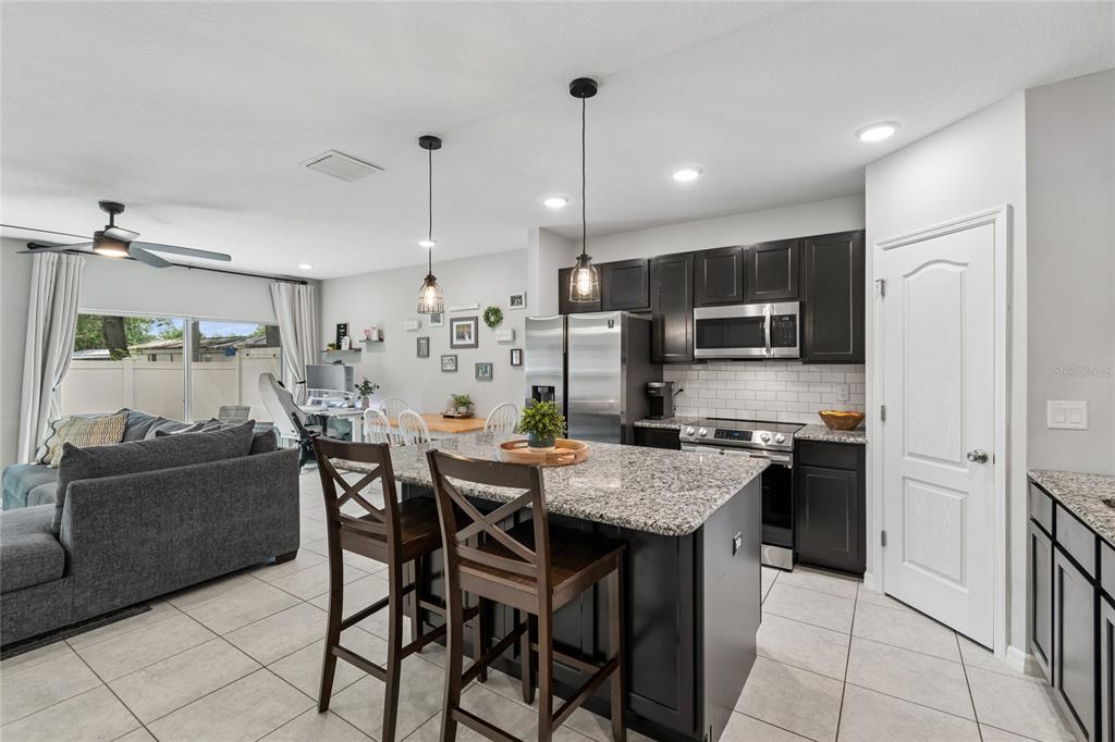 A kitchen with dark cabinets, granite countertops, and an island opens into a living area — 4733 DEER TRACK STREET, TAMPA, FL