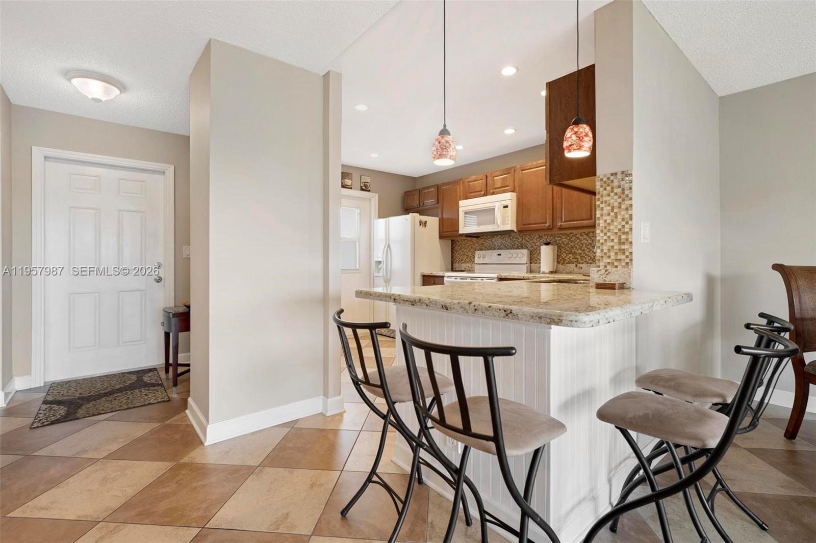 A kitchen features a granite-topped breakfast bar, wooden cabinets, and tile flooring — 1000 NE 14th Ave # 602, Hallandale Beach FL 33009, HALLANDALE BEACH, FL