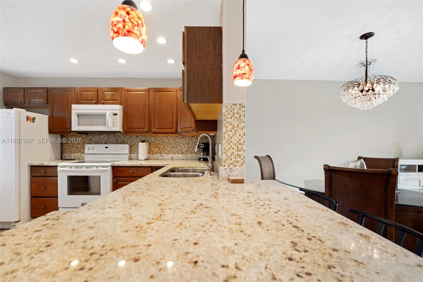 A kitchen features wood cabinets, granite countertops, a tile backsplash, and a dining area — 1000 NE 14th Ave # 602, Hallandale Beach FL 33009, HALLANDALE BEACH, FL