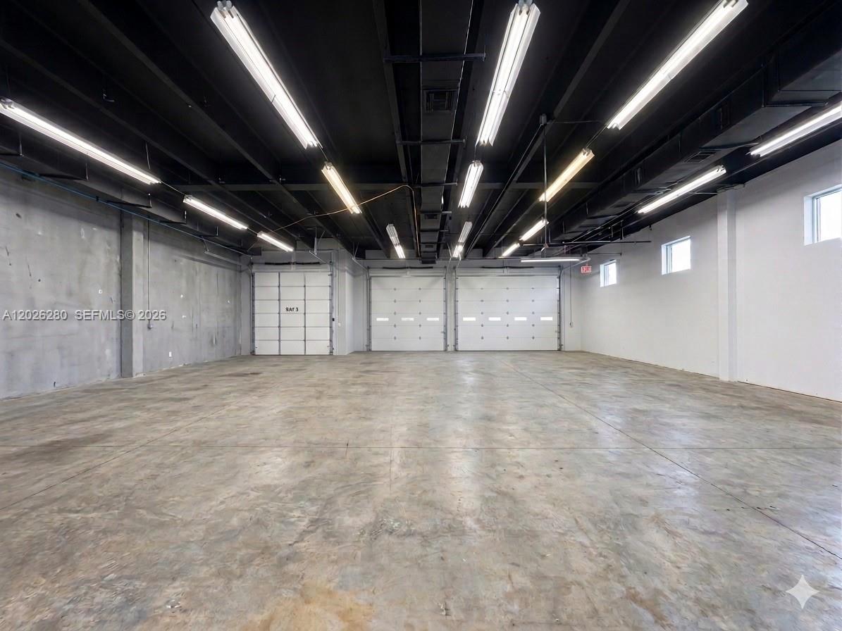 An empty industrial warehouse space features a concrete floor, exposed ceiling, and three roll-up doors — 590 SW 9th Ter # 11, Pompano Beach FL 33069, POMPANO BEACH, FL