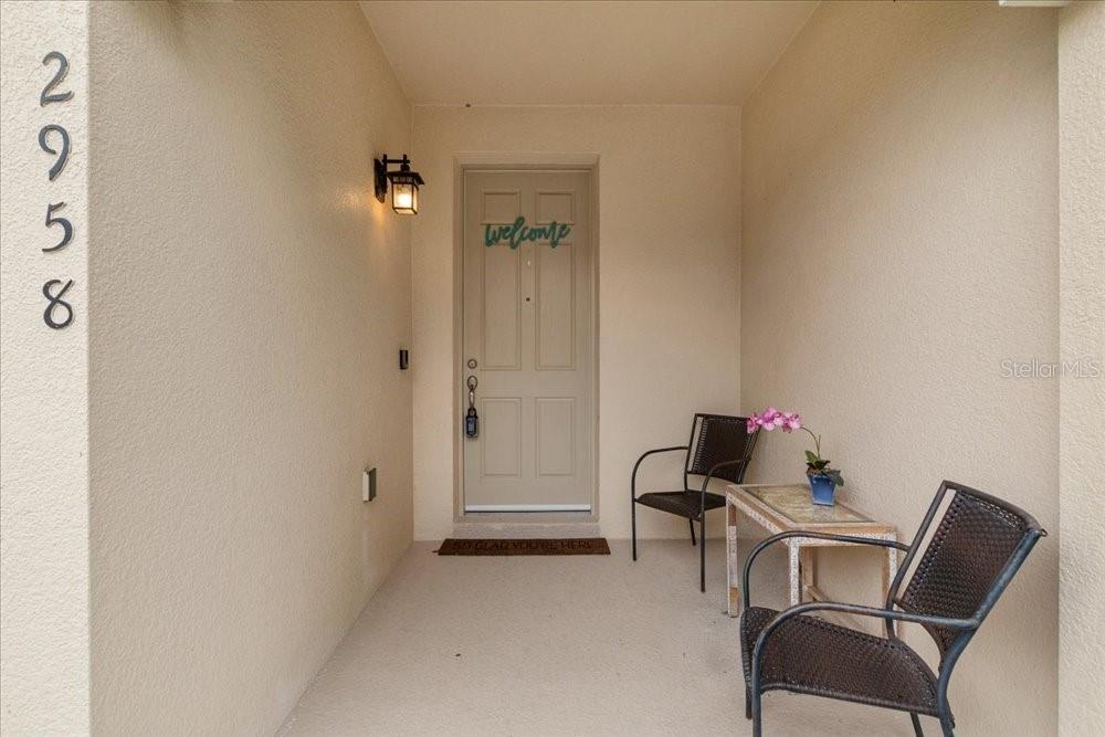 A covered entryway features a beige door, two chairs, a small table, and house numbers — 2958 AQUA VIRGO LOOP UNIT 52, ORLANDO, FL