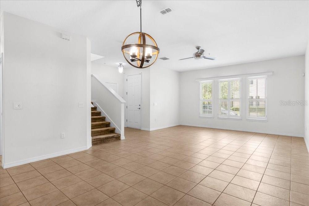An open living area features tile flooring, a wooden orb chandelier, and a carpeted staircase — 2958 AQUA VIRGO LOOP UNIT 52, ORLANDO, FL