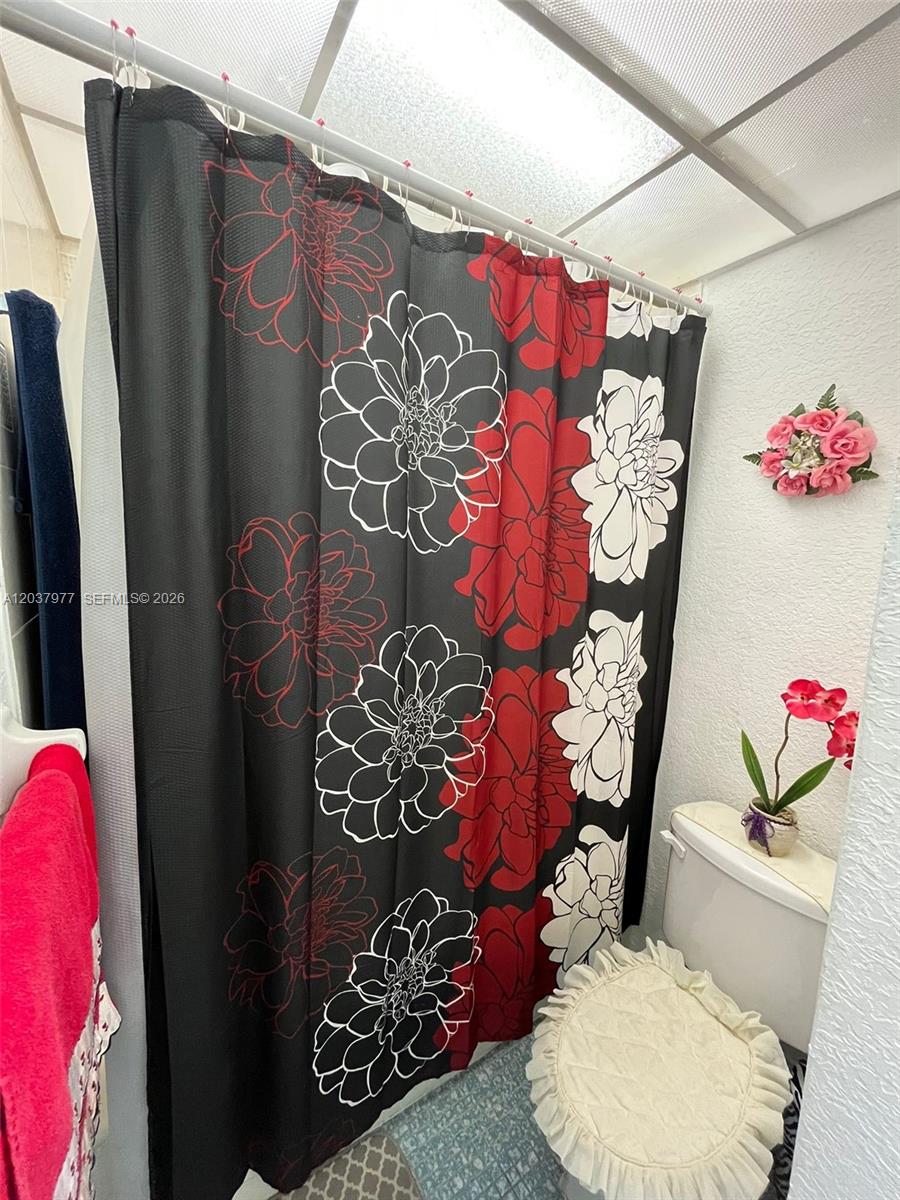 A bathroom features a floral shower curtain, a toilet with a ruffled cover, and wall decor — 525 W 69th St # 207, Hialeah FL 33014, HIALEAH, FL