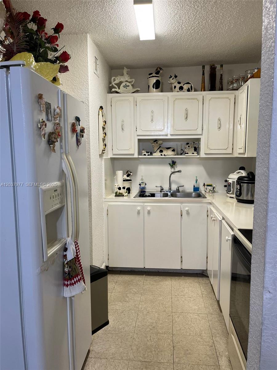 A galley kitchen features white cabinets, a double sink, and a white refrigerator — 525 W 69th St # 207, Hialeah FL 33014, HIALEAH, FL