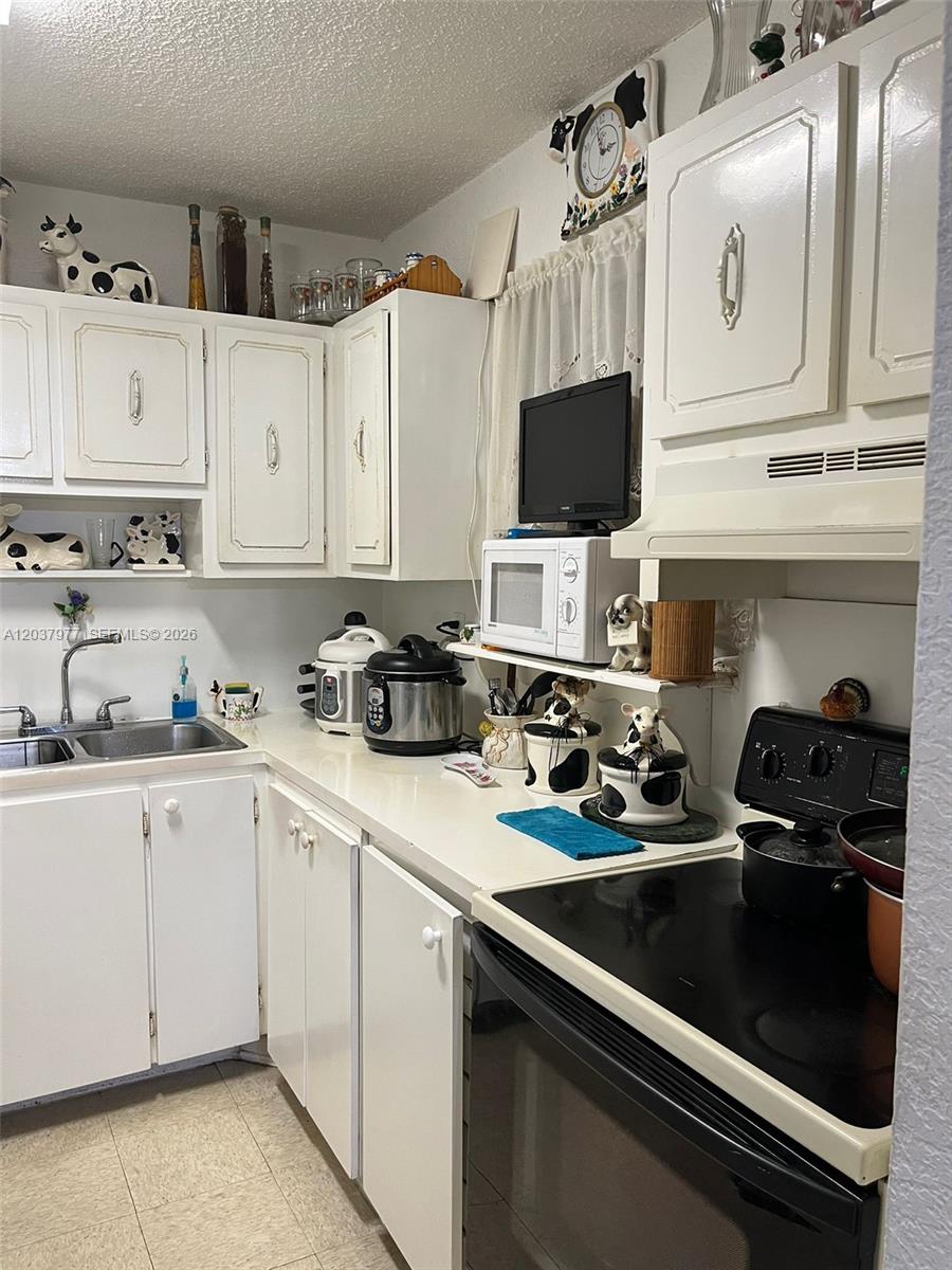 A kitchen features white cabinets, a black stove, a microwave, and cow-themed decor — 525 W 69th St # 207, Hialeah FL 33014, HIALEAH, FL