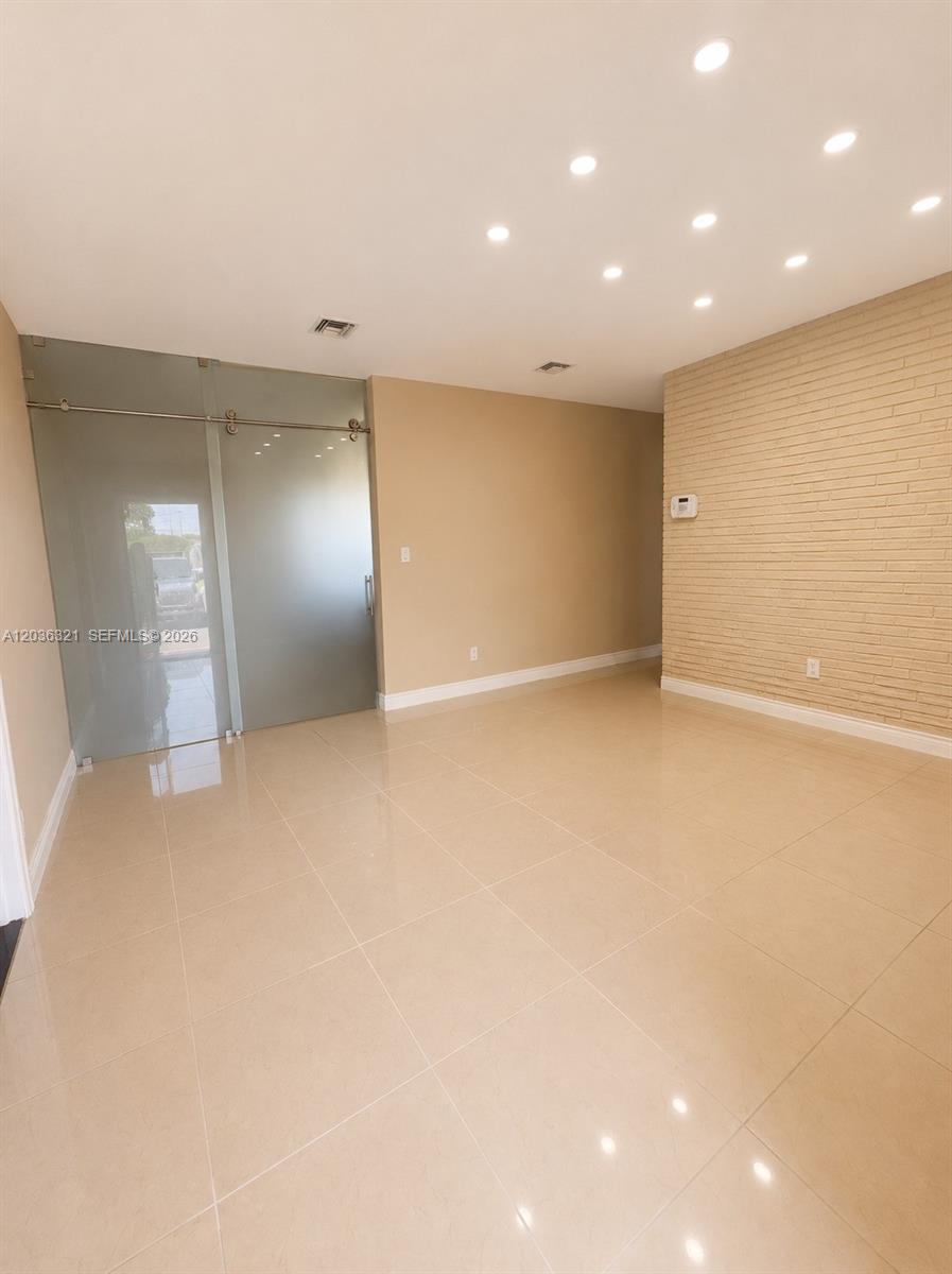 A room with beige tile flooring, a textured brick wall, and a frosted glass sliding door — 4011 SW 28th St # 0, West Park FL 33023, WEST PARK, FL