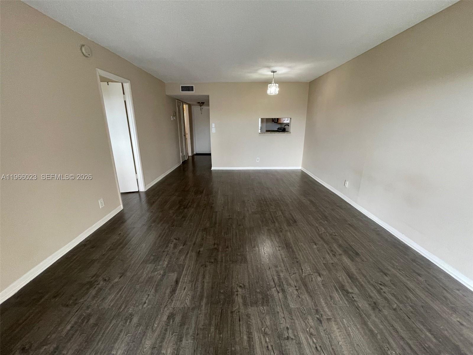 An empty living room features dark wood-look flooring, beige walls, and a small pass-through window — 4700 Washington St # 507, Hollywood FL 33021, HOLLYWOOD, FL