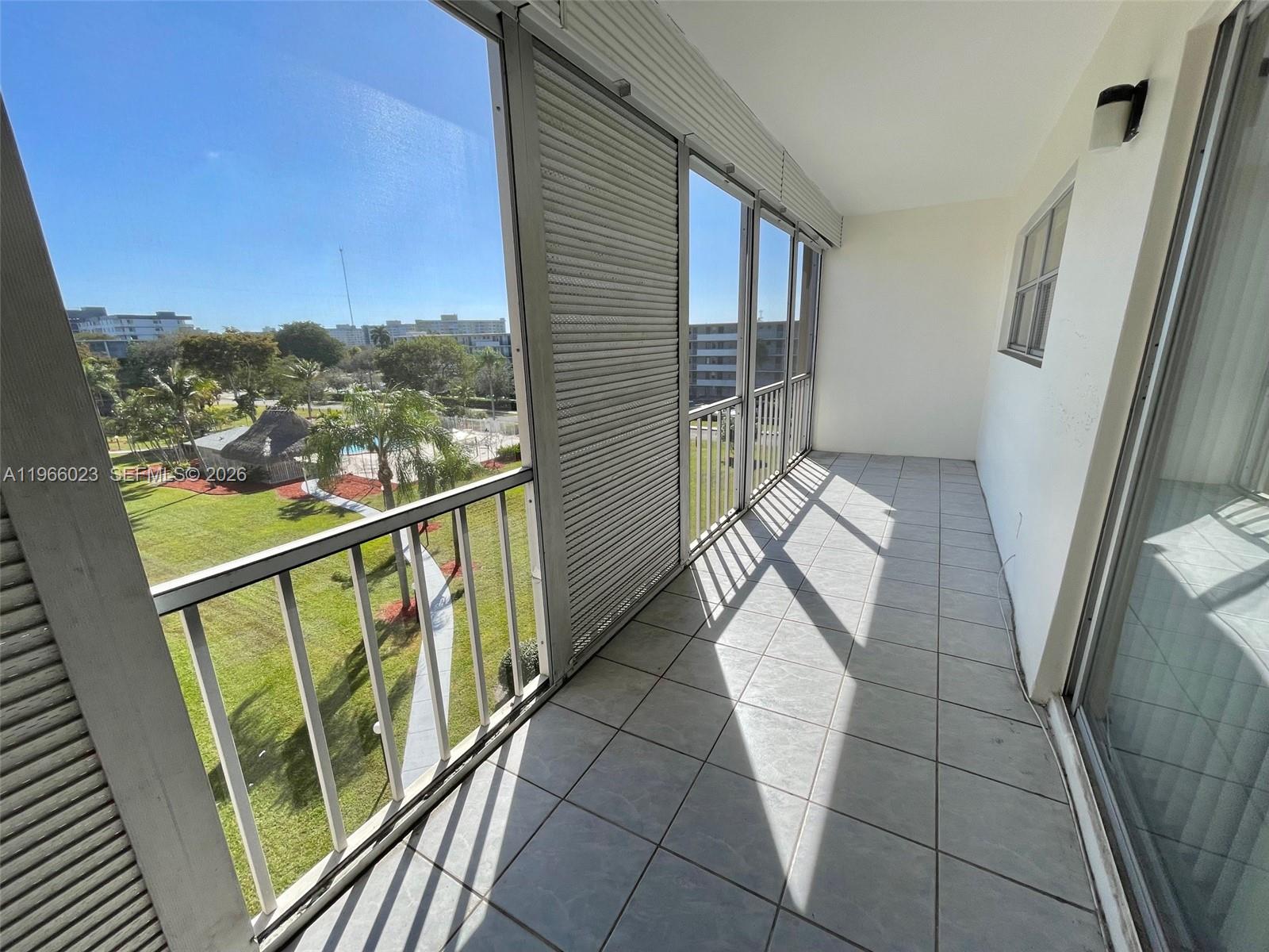 A tiled balcony features metal railings and roll-down shutters overlooking a grassy courtyard area — 4700 Washington St # 507, Hollywood FL 33021, HOLLYWOOD, FL