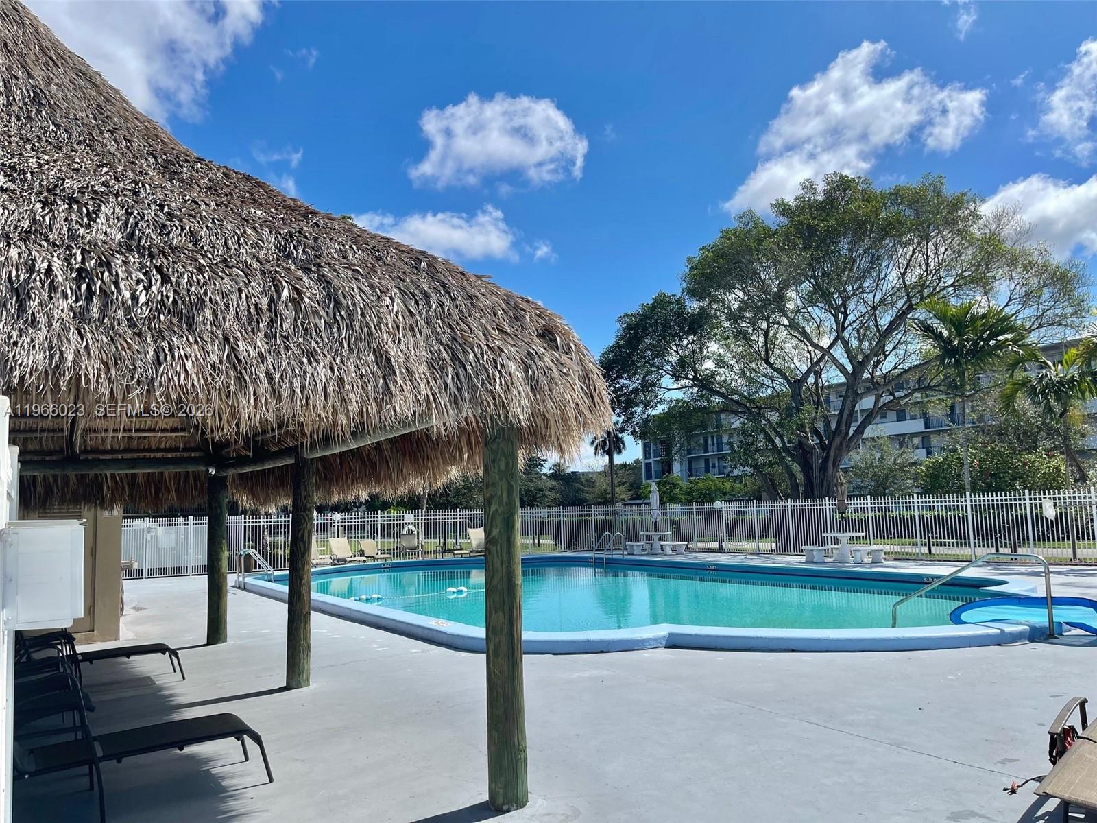 A swimming pool with a tiki hut and lounge chairs under a blue sky — 4700 Washington St # 507, Hollywood FL 33021, HOLLYWOOD, FL