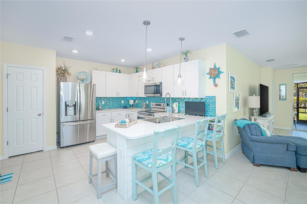 A kitchen features white cabinets, a blue tiled backsplash, a central island, and stainless appliances — 25104 E LENOX CIRCLE, PUNTA GORDA, FL