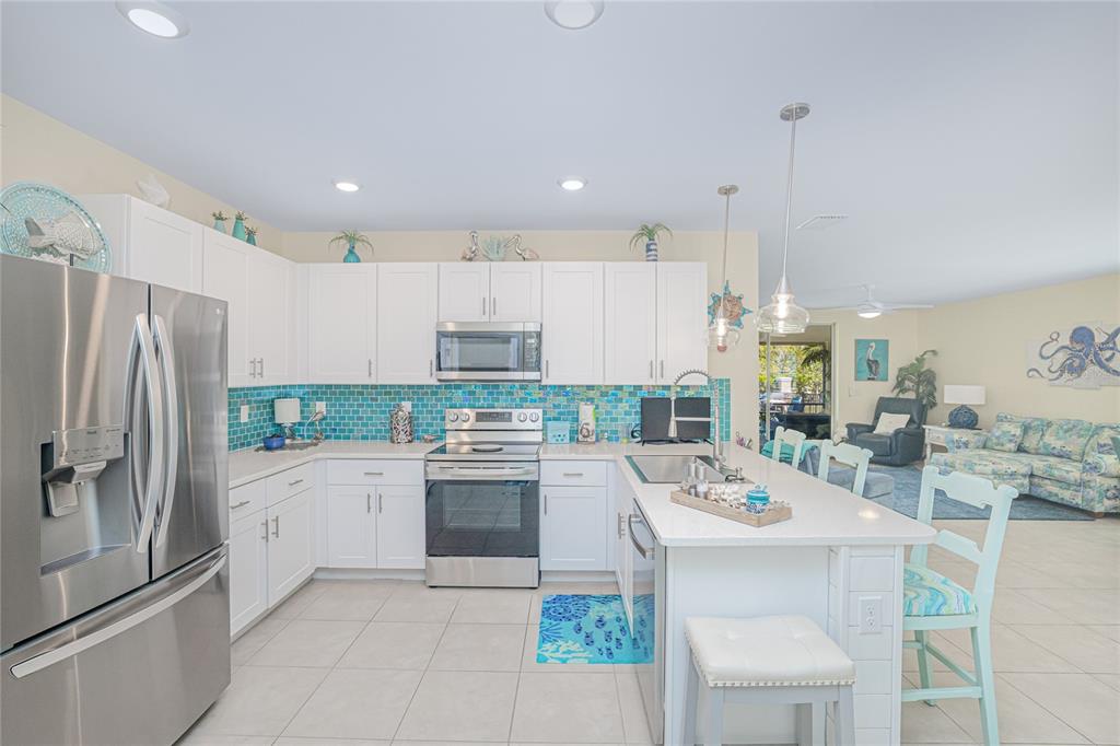 A kitchen features white cabinets, stainless steel appliances, and a blue glass tile backsplash — 25104 E LENOX CIRCLE, PUNTA GORDA, FL