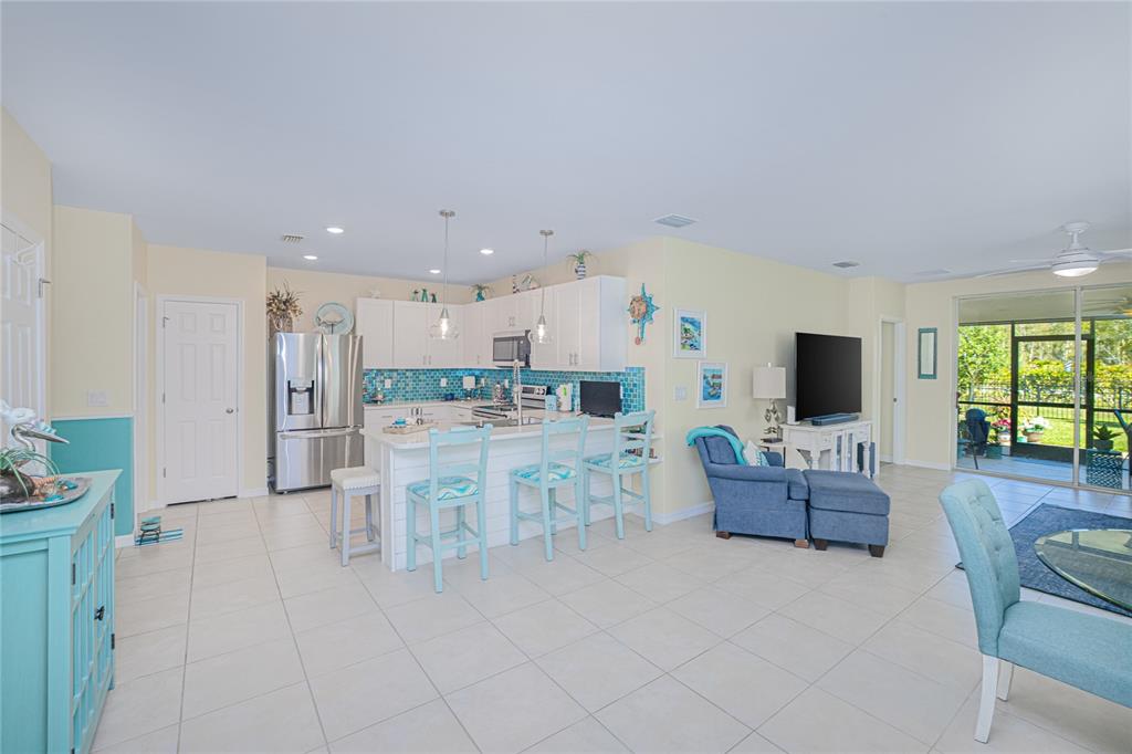 An open-concept kitchen and living area features white cabinetry, blue tile backsplashes, and tile flooring — 25104 E LENOX CIRCLE, PUNTA GORDA, FL