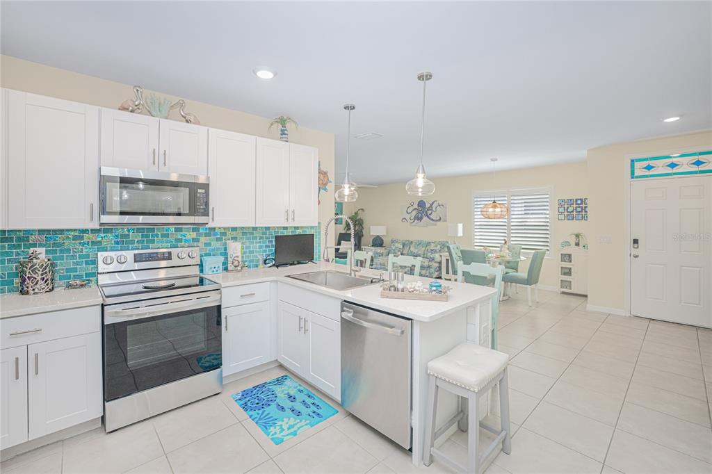 A bright kitchen features white cabinets, a blue tiled backsplash, and a stainless steel island — 25104 E LENOX CIRCLE, PUNTA GORDA, FL