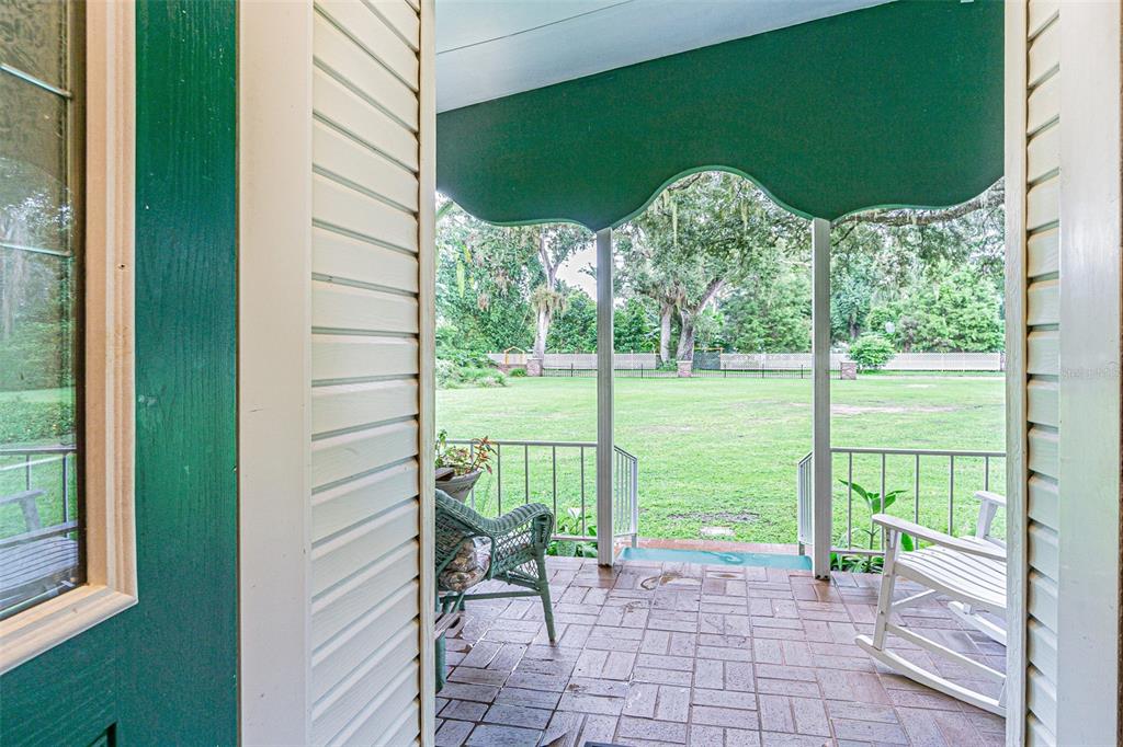 A covered brick patio overlooks a large grassy backyard with trees and a fence — 3349 OAKWOOD DRIVE, WESLEY CHAPEL, FL