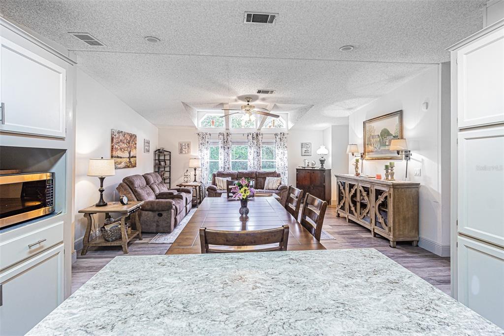 A kitchen island overlooks a dining area and living room with brown furniture and windows — 3349 OAKWOOD DRIVE, WESLEY CHAPEL, FL