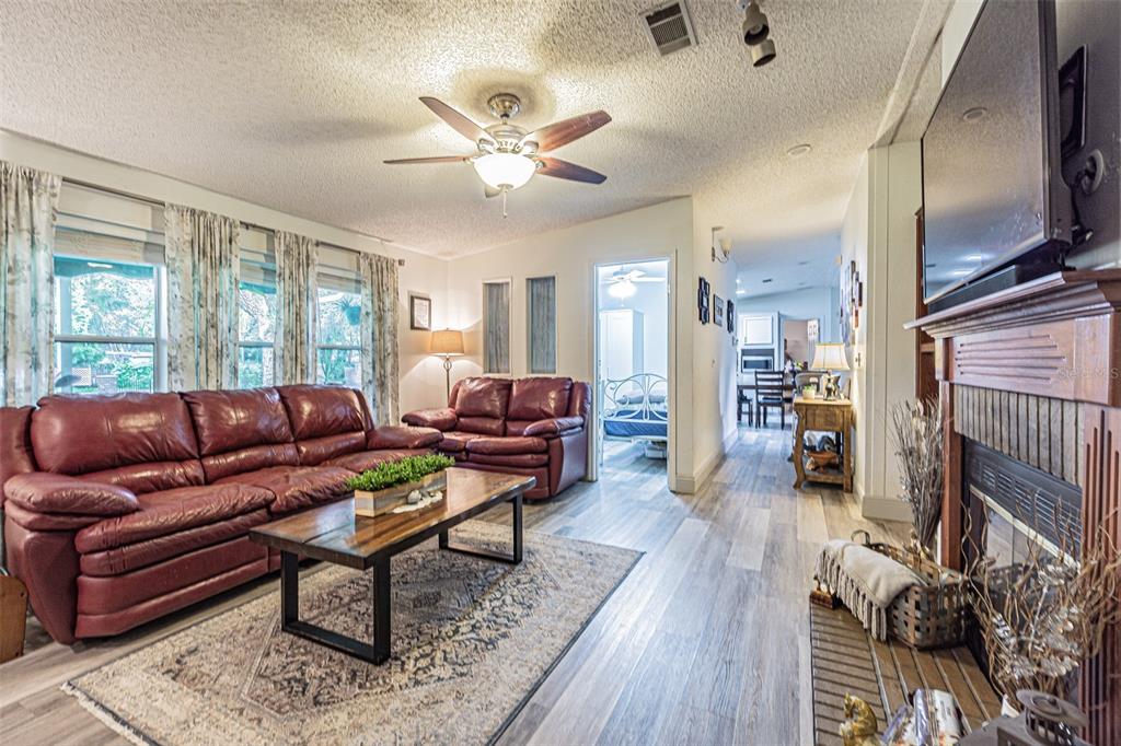 A living room features a red leather sofa, wood-look flooring, a fireplace, and a ceiling fan — 3349 OAKWOOD DRIVE, WESLEY CHAPEL, FL