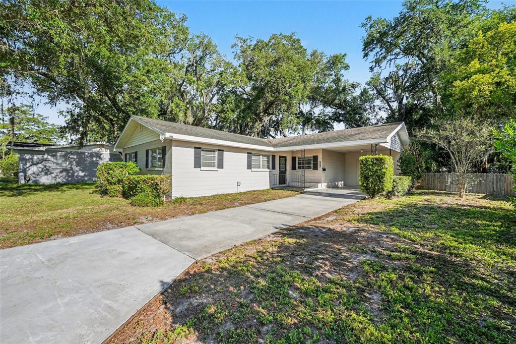 A single-story house with light siding, a concrete driveway, and a carport under large trees — 521 W PALMEDEN DRIVE, LAKELAND, FL