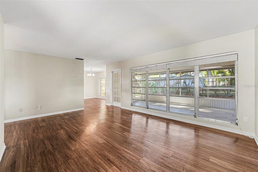 A living room with wood-look flooring, white walls, and a large window overlooking a porch — 521 W PALMEDEN DRIVE, LAKELAND, FL
