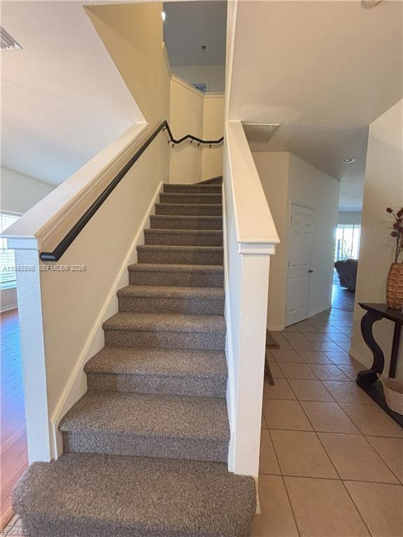 A carpeted staircase leads to an upper level in a home with tiled flooring — 8042 Silver Birch Way, Lehigh Acres FL 33971, LEHIGH ACRES, FL