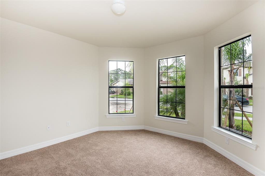An empty bedroom features beige carpet, neutral walls, and three windows with black frames — 2558 SHERMAN OAK DRIVE, NORTH PORT, FL