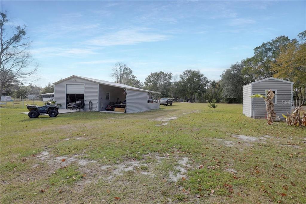 A large metal workshop with an attached carport stands on a grassy residential lot — 5336 SW COUNTY ROAD 791, LAKE BUTLER, FL