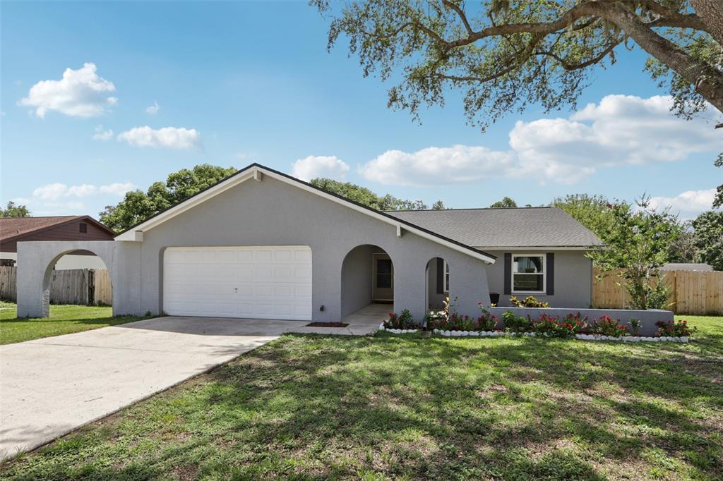 A single-story gray house features a white garage door, arched entryway, and a front lawn — 1009 BLACK KNIGHT DRIVE, VALRICO, FL