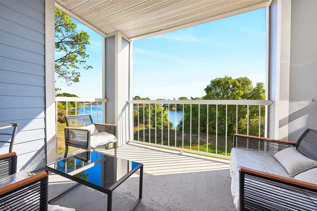 A covered balcony features outdoor furniture and a view of a lake and trees — 2569 GRASSY POINT DRIVE UNIT 207, LAKE MARY, FL