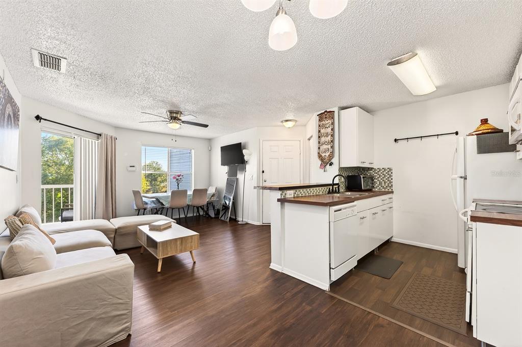 An open-concept living room and kitchen featuring wood-look flooring, white cabinetry, and a dining area — 2569 GRASSY POINT DRIVE UNIT 207, LAKE MARY, FL