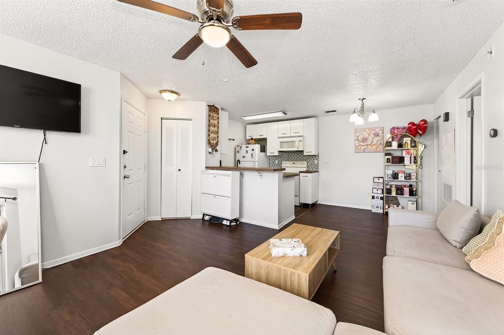 A living room with dark wood floors, a ceiling fan, and an open kitchen area — 2569 GRASSY POINT DRIVE UNIT 207, LAKE MARY, FL