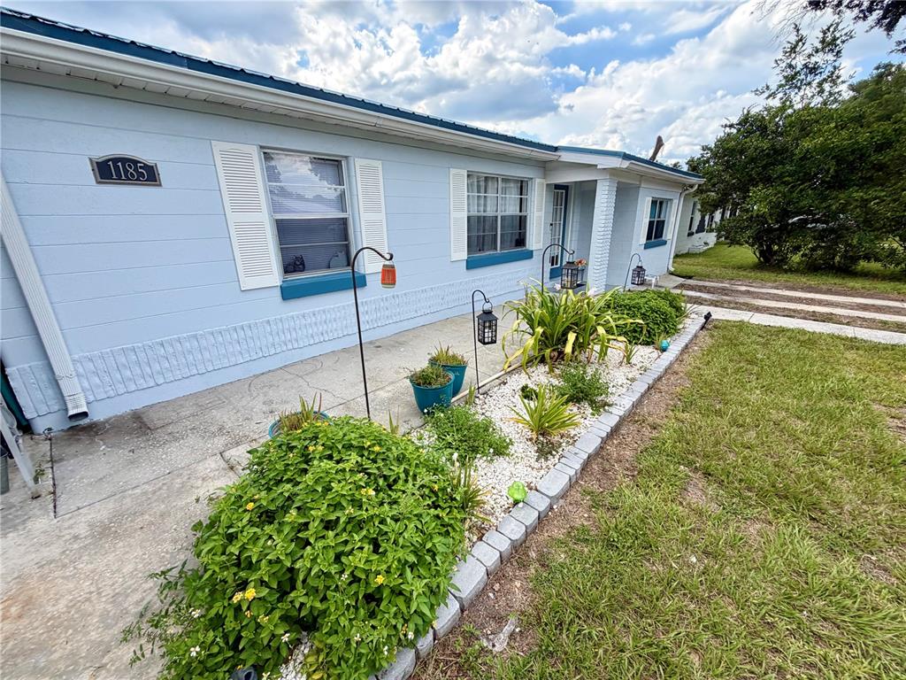 A light blue house exterior features white shutters, a concrete walkway, and a landscaped garden — 1185 S JOHNSON AVENUE, BARTOW, FL