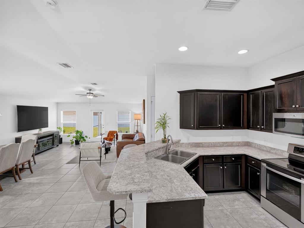 An open-concept kitchen with dark cabinets and granite countertops overlooks a living and dining area — 14453 BARLEY FIELD DRIVE, WIMAUMA, FL