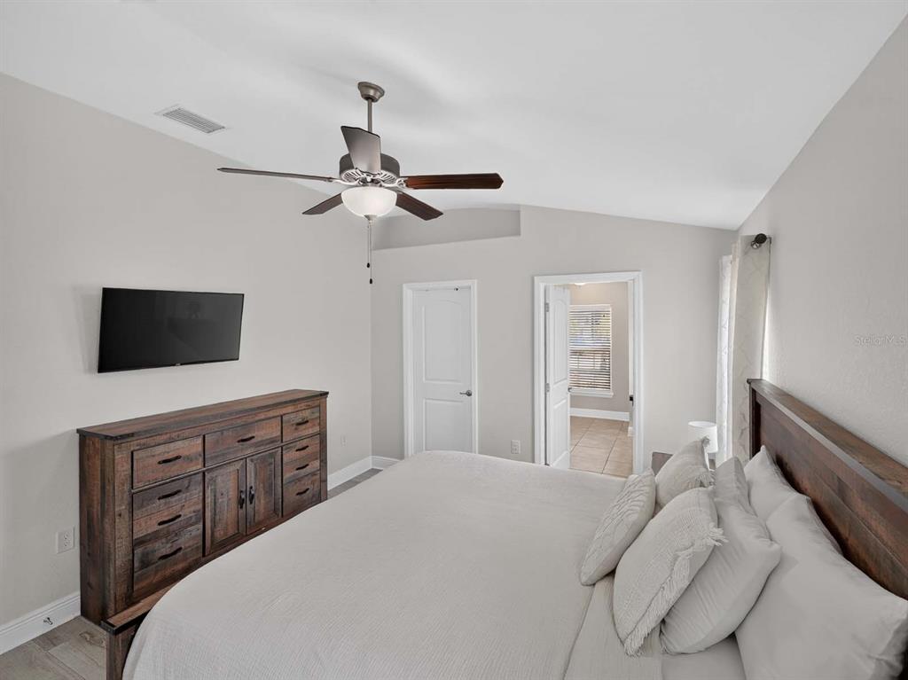A bedroom features a wooden dresser, a large bed with white bedding, and a ceiling fan — 14453 BARLEY FIELD DRIVE, WIMAUMA, FL
