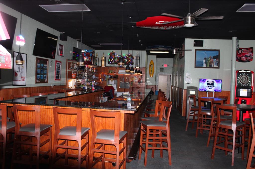 A bar interior features a long counter with wooden stools, pendant lighting, and a dartboard — 6636 RIDGE ROAD, PORT RICHEY, FL