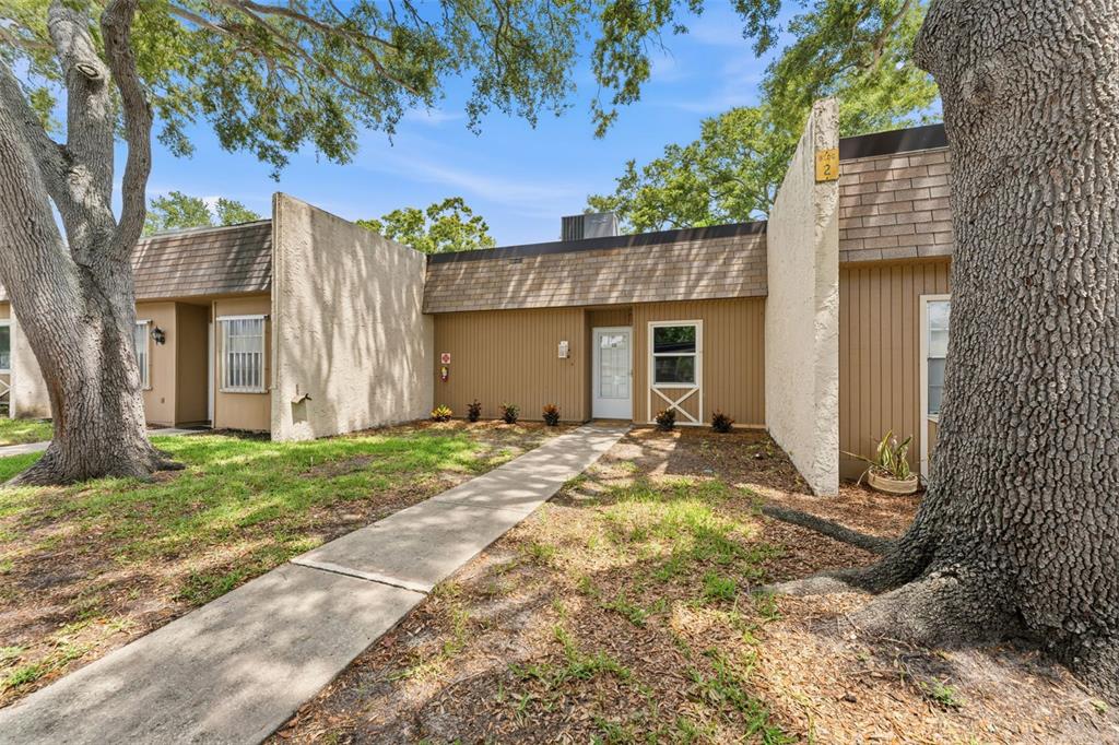 A sidewalk leads to the entrance of a single-story tan building with wood-paneled siding — 11511 113TH STREET UNIT 2D, LARGO, FL