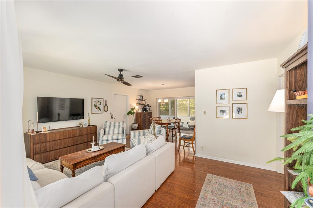 A living room with hardwood floors, a white sectional sofa, and a dining area beyond — 3224 NW 31ST AVENUE, GAINESVILLE, FL