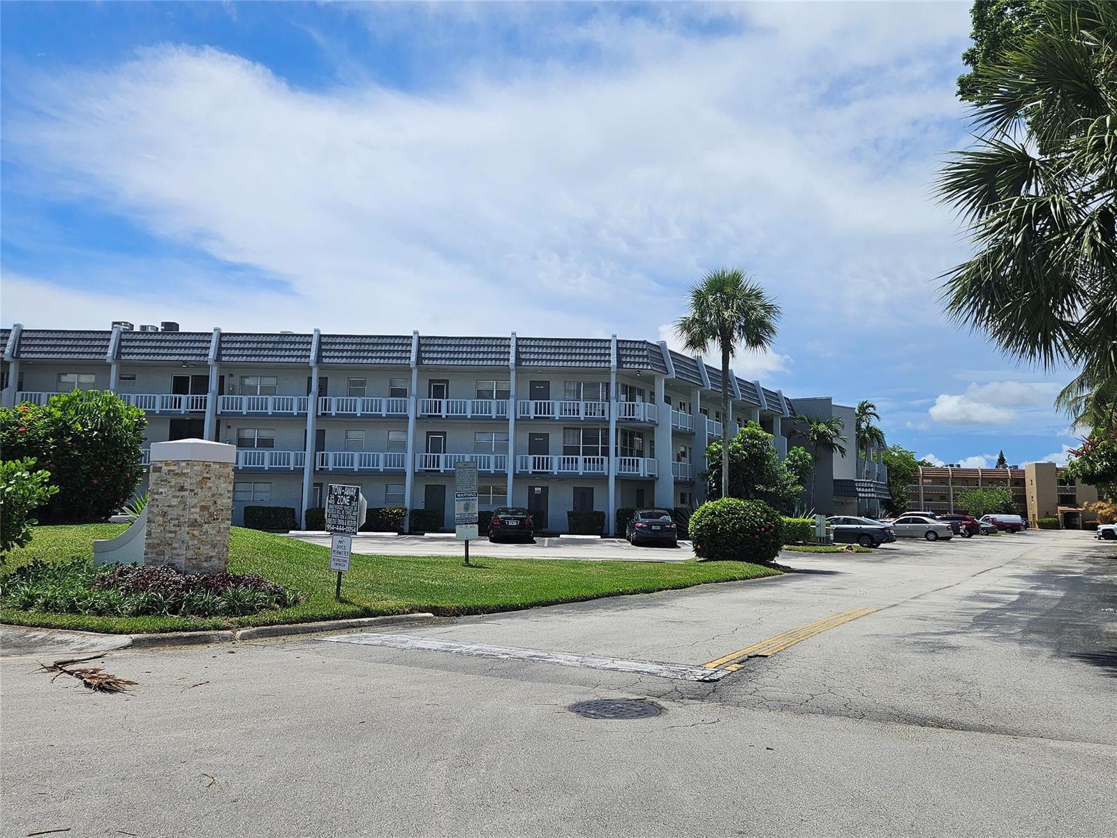 A three-story apartment building with a parking lot and palm trees under a blue sky — 6650 Royal Palm Boulevard # 315c, Margate FL 33063, MARGATE, FL